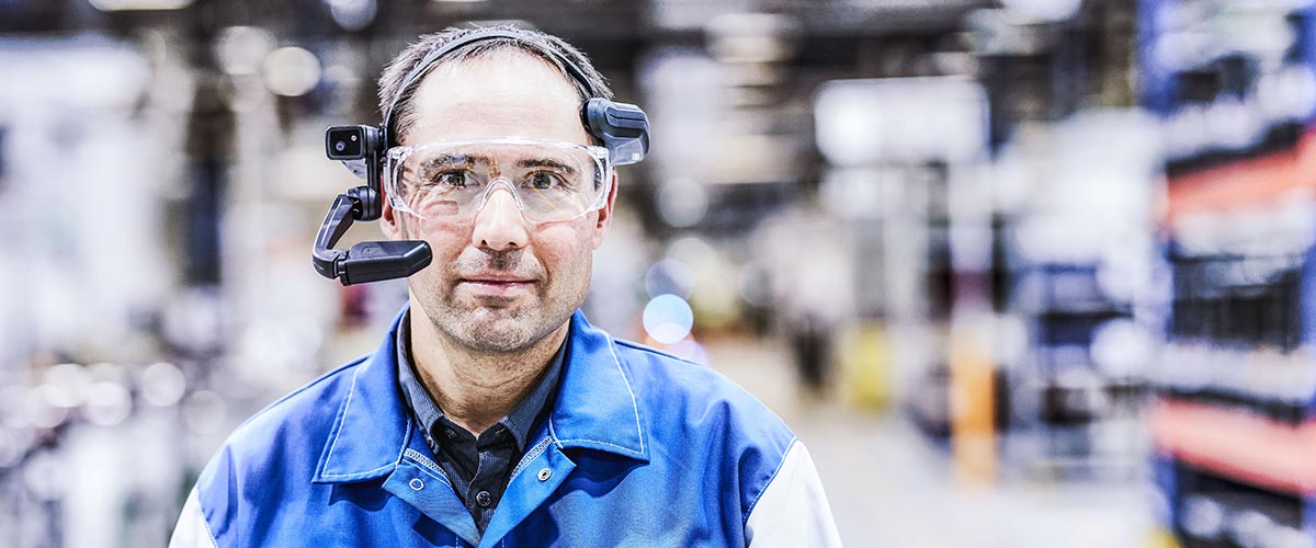 Ein Mann mit einer Augmented Reality Brille, im Hintergrund Produktionsumfeld von Purem by Eberspächer